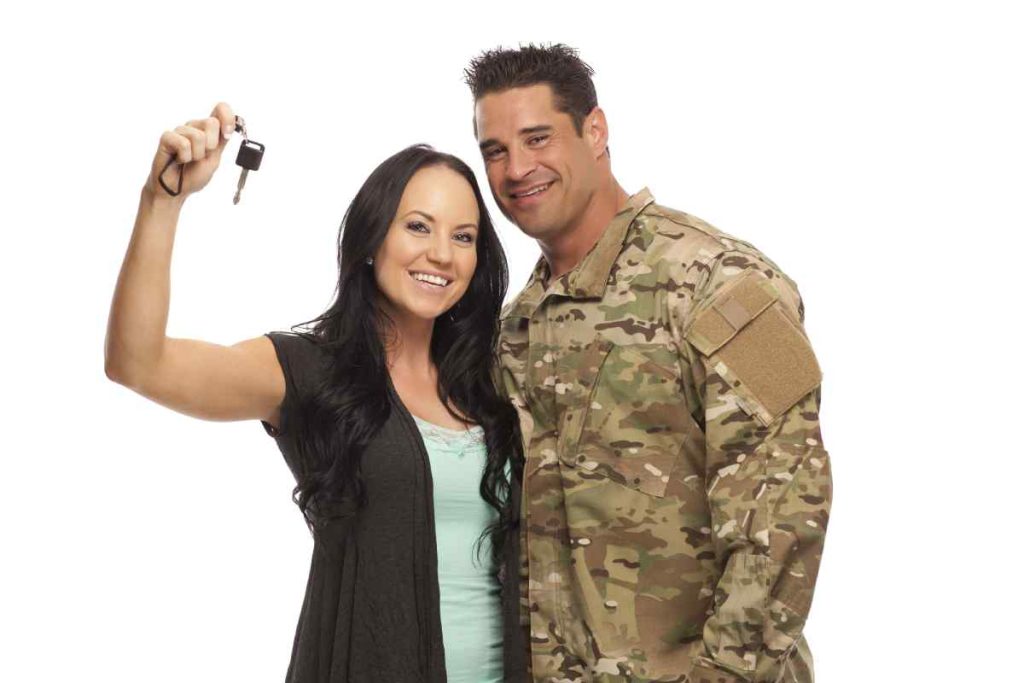 A military couple smiles and holds up the keys to their new car