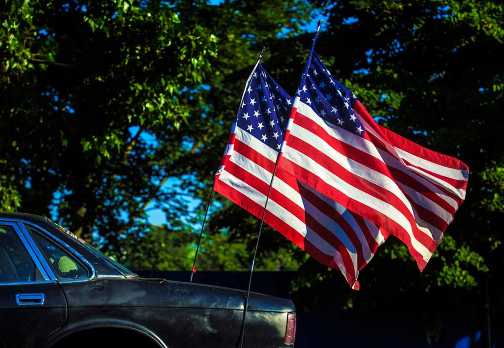Two Memorial Day flags flying off the back of a vintage Chevy vehicle