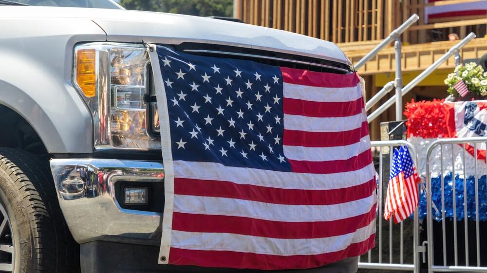 A truck with an American Flag tied to the bumper 